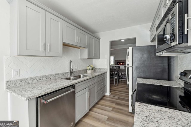 kitchen featuring light stone countertops, light hardwood / wood-style floors, sink, tasteful backsplash, and appliances with stainless steel finishes