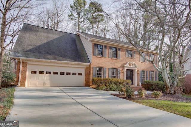 colonial home featuring an attached garage, driveway, a shingled roof, and brick siding