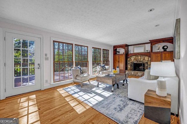 living area with visible vents, wood finished floors, crown molding, a textured ceiling, and a fireplace