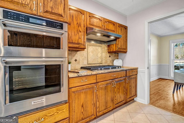 kitchen with stainless steel appliances, brown cabinets, under cabinet range hood, and light tile patterned floors