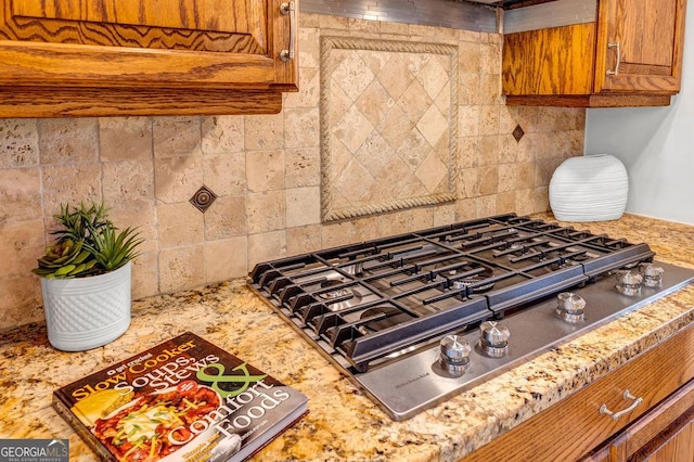 room details with tasteful backsplash, brown cabinets, stainless steel gas stovetop, and light stone countertops