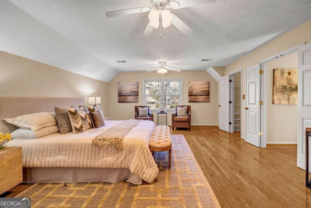 bedroom with visible vents, baseboards, lofted ceiling, wood finished floors, and a textured ceiling