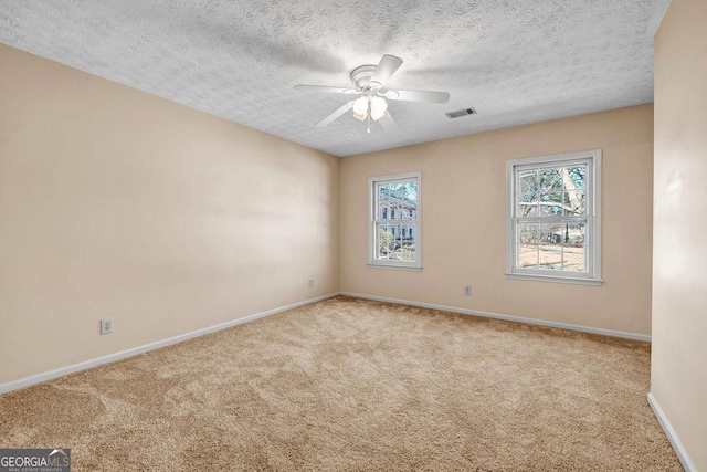 carpeted empty room featuring ceiling fan, a textured ceiling, visible vents, and baseboards