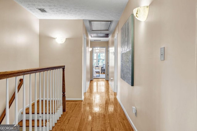 hallway featuring attic access, baseboards, wood finished floors, a textured ceiling, and an upstairs landing