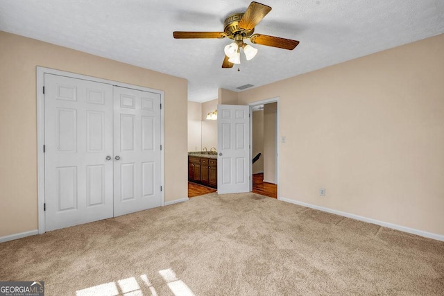 unfurnished bedroom featuring a textured ceiling, a sink, baseboards, a closet, and carpet