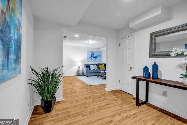 corridor featuring visible vents, light wood-style flooring, and baseboards