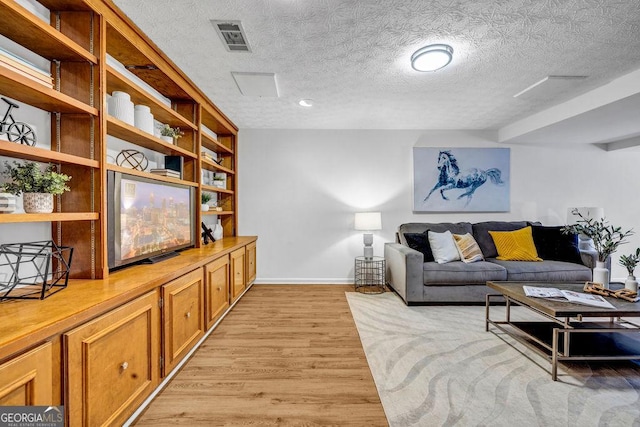 living room featuring a textured ceiling, light wood-style flooring, visible vents, and baseboards