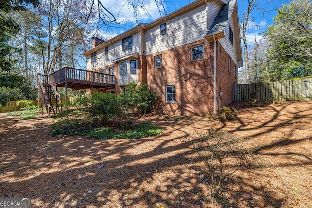 back of house with brick siding, fence, stairs, a wooden deck, and a chimney