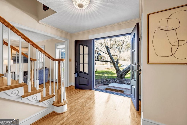 entryway featuring crown molding, light wood-style flooring, a textured ceiling, baseboards, and stairs