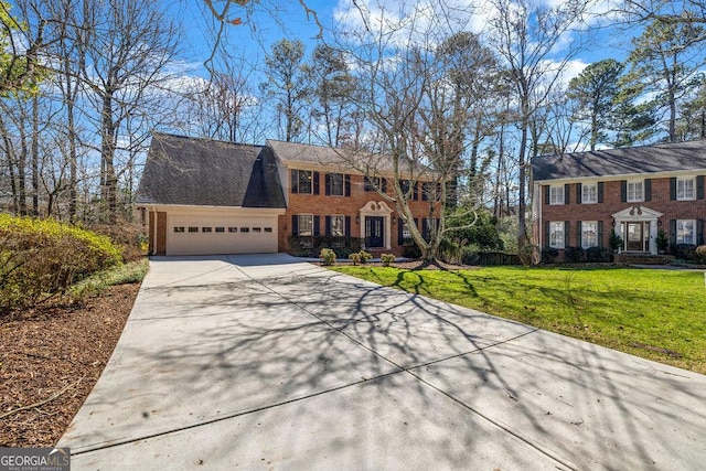 colonial inspired home featuring an attached garage, a front yard, concrete driveway, and brick siding