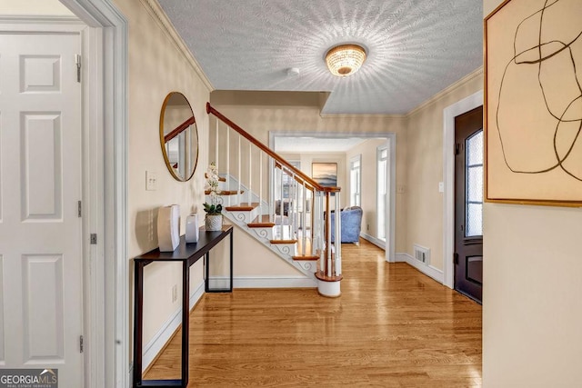 foyer featuring a textured ceiling, wood finished floors, visible vents, stairs, and crown molding