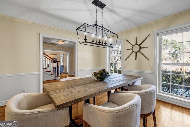 dining area with stairway, wainscoting, wood finished floors, and crown molding