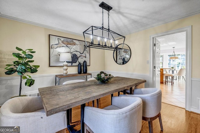 dining space featuring visible vents, a wainscoted wall, wood finished floors, crown molding, and a textured ceiling