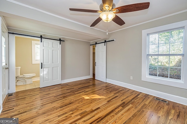 unfurnished bedroom with hardwood / wood-style floors, ensuite bathroom, ceiling fan, a barn door, and ornamental molding