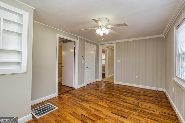 empty room featuring crown molding, wood-type flooring, built in shelves, and ceiling fan