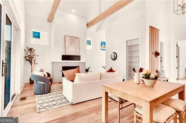 living room with a notable chandelier, light wood-type flooring, beamed ceiling, and a high ceiling