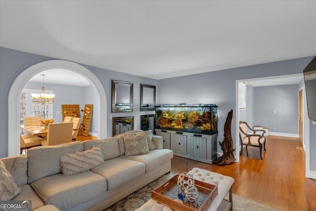 living area featuring arched walkways, a notable chandelier, light wood-style flooring, and baseboards