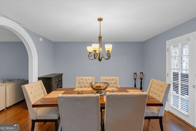 dining space featuring arched walkways, a notable chandelier, and wood finished floors