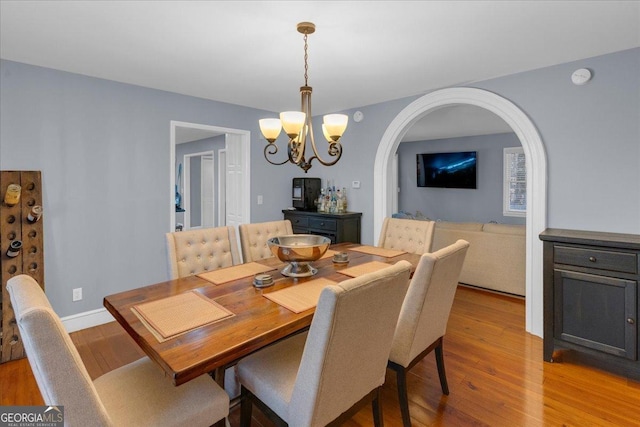 dining space with light wood finished floors, baseboards, arched walkways, and an inviting chandelier