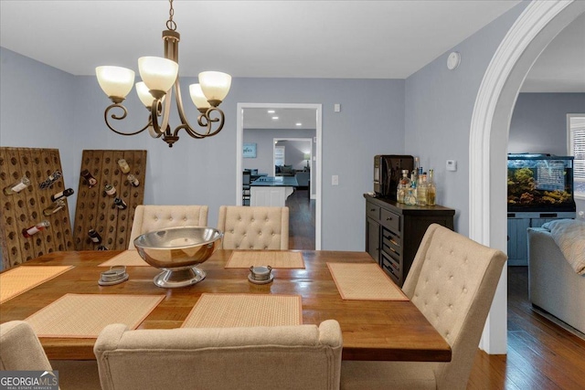 dining area with arched walkways, wood finished floors, and a notable chandelier