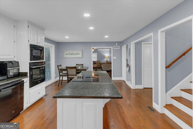 kitchen featuring light wood finished floors, recessed lighting, white cabinetry, a kitchen island, and black appliances