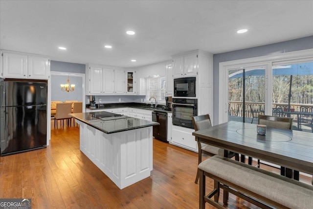 kitchen with a kitchen bar, dark countertops, white cabinetry, and black appliances