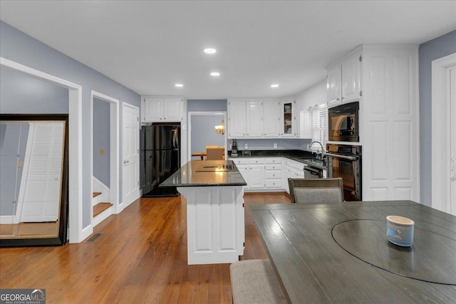 kitchen featuring dark wood-style floors, a center island, dark countertops, white cabinetry, and black appliances