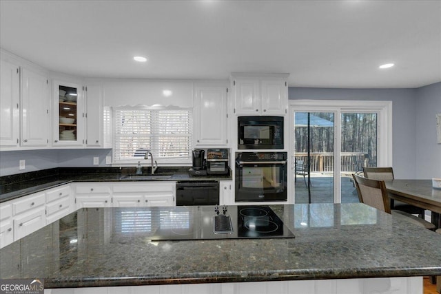 kitchen featuring glass insert cabinets, a center island, black appliances, white cabinetry, and a sink