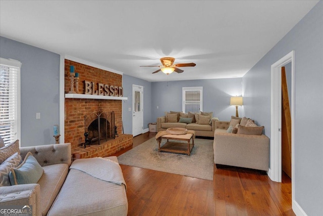 living area featuring a brick fireplace, baseboards, a ceiling fan, and wood finished floors