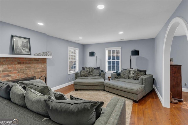 living area featuring arched walkways, a brick fireplace, wood finished floors, and baseboards