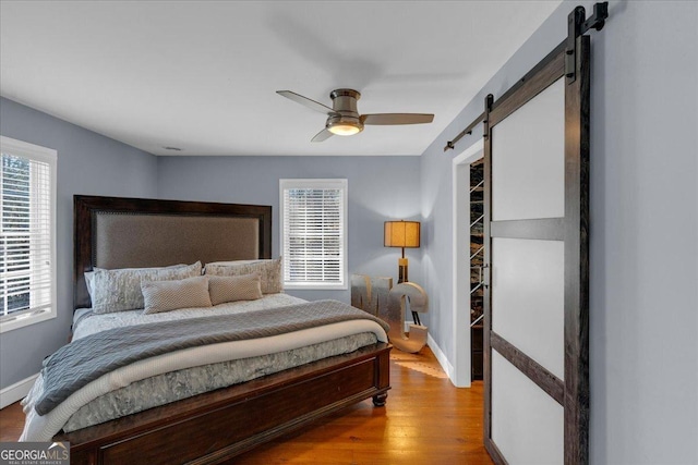 bedroom featuring light wood finished floors, a barn door, a ceiling fan, and baseboards