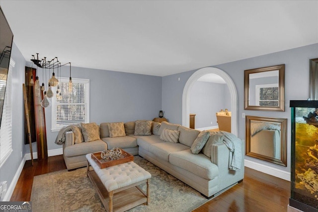 living room featuring arched walkways, a healthy amount of sunlight, baseboards, and wood finished floors