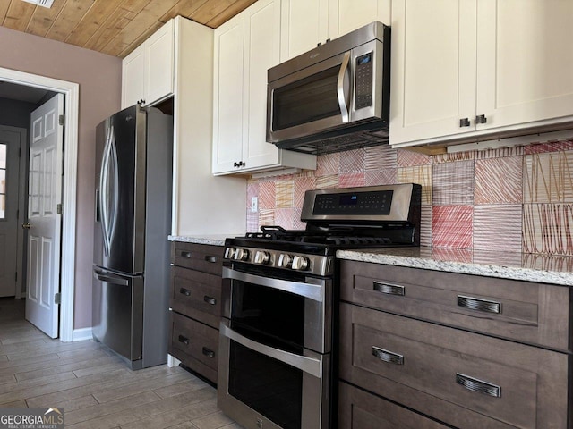 kitchen with white cabinets, stainless steel appliances, backsplash, and light stone countertops