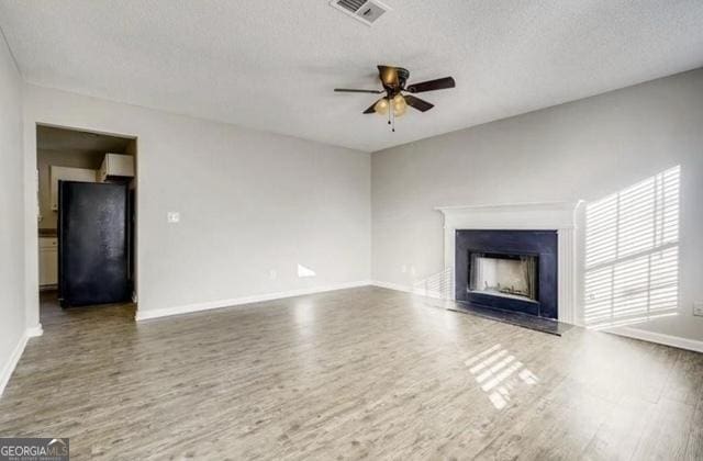 unfurnished living room with visible vents, a fireplace, a ceiling fan, and wood finished floors