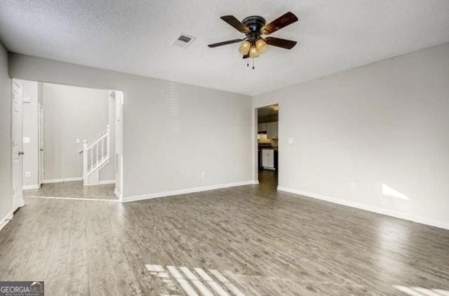 unfurnished living room with visible vents, wood finished floors, a ceiling fan, and stairway