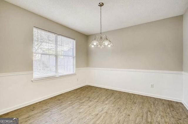 empty room featuring a chandelier, a textured ceiling, baseboards, and wood finished floors