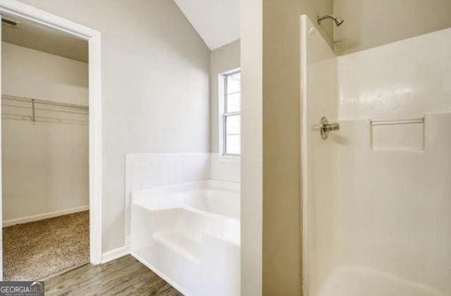 full bathroom with wood finished floors, lofted ceiling, a shower stall, a walk in closet, and a garden tub