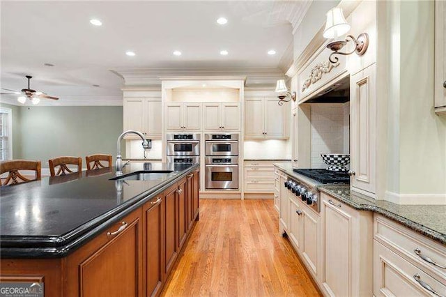 kitchen featuring dark stone countertops, sink, stainless steel appliances, an island with sink, and ornamental molding