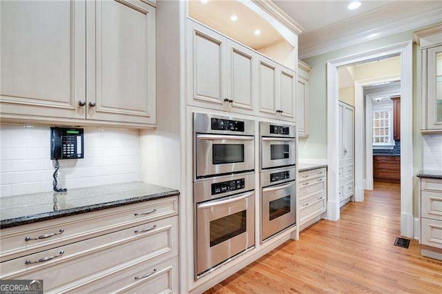 kitchen with ornamental molding, dark stone countertops, cream cabinets, and stainless steel double oven