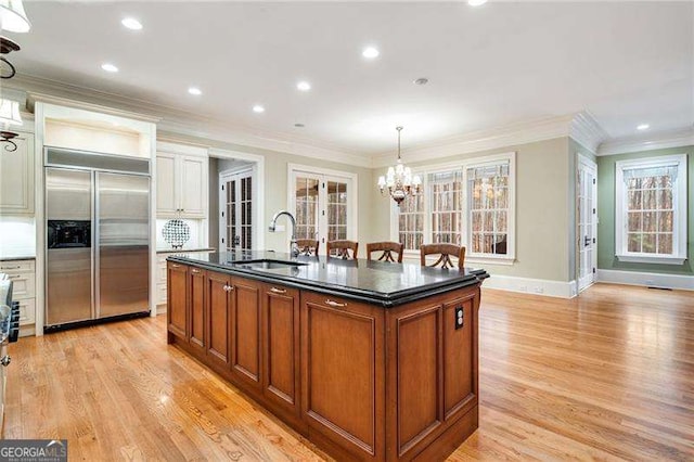 kitchen with an island with sink, decorative light fixtures, a wealth of natural light, built in fridge, and sink