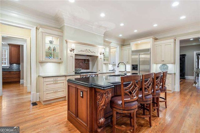 kitchen featuring a center island with sink, a kitchen bar, sink, stainless steel built in fridge, and cream cabinets