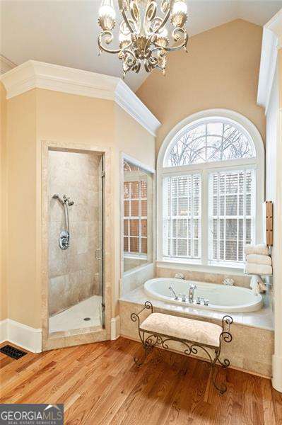 bathroom featuring wood-type flooring, independent shower and bath, crown molding, vaulted ceiling, and an inviting chandelier