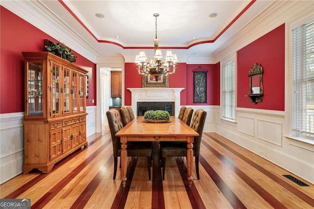 dining space with a notable chandelier, ornamental molding, a raised ceiling, and wood-type flooring