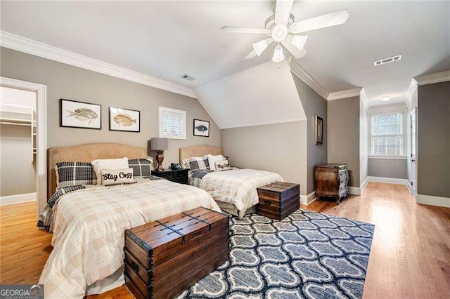 bedroom featuring ceiling fan, ornamental molding, light wood-type flooring, and a spacious closet