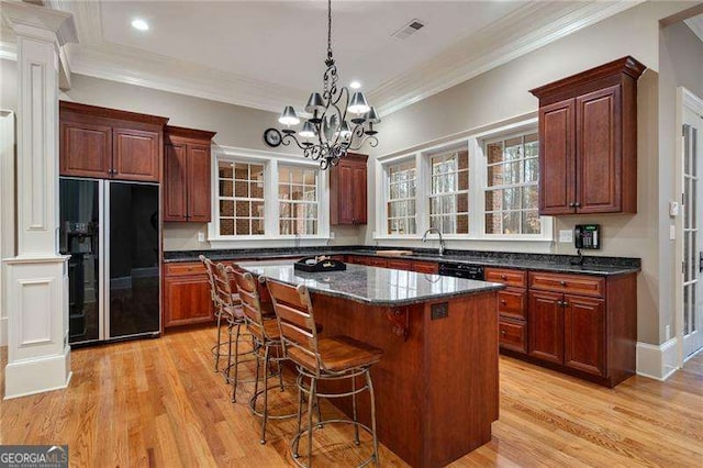 kitchen with light hardwood / wood-style floors, black fridge, decorative columns, and a center island