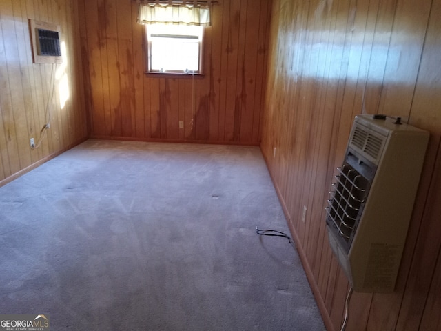 carpeted spare room with heating unit, wooden walls, and a wall mounted air conditioner