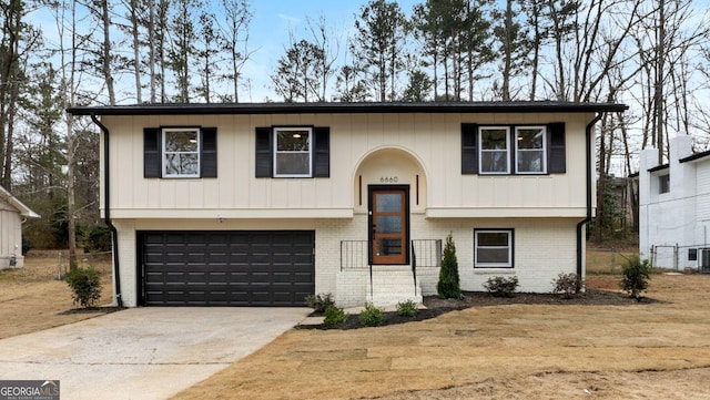 raised ranch featuring driveway, brick siding, an attached garage, and fence