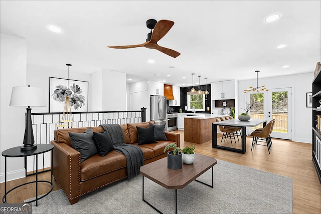 living room featuring light wood-type flooring, baseboards, ceiling fan with notable chandelier, and recessed lighting