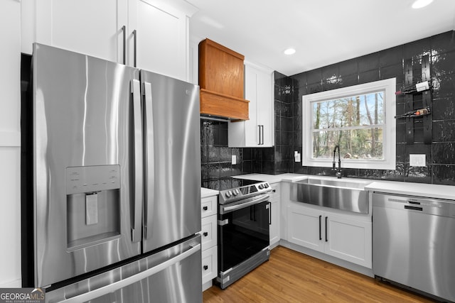 kitchen featuring a sink, white cabinets, light wood-style floors, appliances with stainless steel finishes, and backsplash