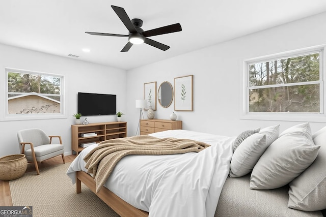 bedroom with a ceiling fan, multiple windows, visible vents, and wood finished floors